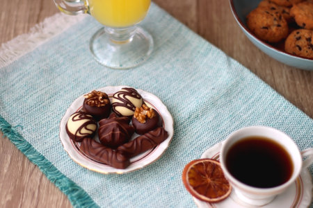 Plate of chocolate pralines, bowl of cookies, cups of tea, glasses of juice and lit candles on the table. Selective focus.の写真素材