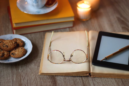 Cup of tea or coffee, plate of cookies, books, e-reader, pencil and lit candles on the table....