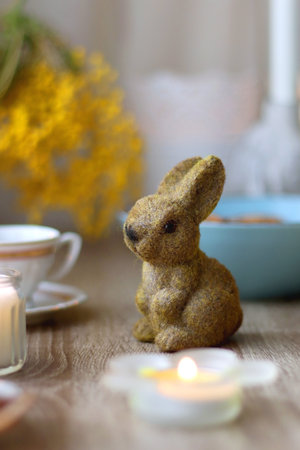 Easter eggs in the basket, bowl of cookies, chocolate pralines, Easter bunny figurine, cups of tea, glasses of juice, flowers and lit candles on the table. Selective focus.の写真素材