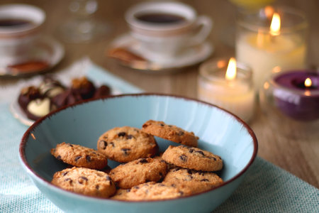 Plate of chocolate pralines, bowl of cookies, cups of tea, glasses of juice and lit candles on the table. Selective focus.の写真素材