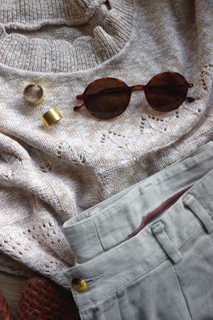 Vintage sweater, neutral trousers, wicker bag, leopard scarf, brown shoes, sunglasses and brass rings on wooden background. Top view.の写真素材