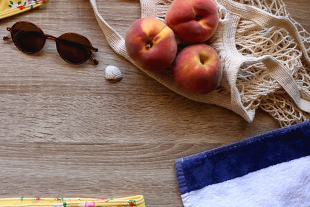Floral bikini, striped beach towel, sunglasses, straw bag, seashell and tote with peaches on wooden background. Top view.の写真素材