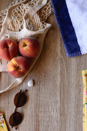 Floral bikini, striped beach towel, sunglasses, straw bag, seashell and tote with peaches on wooden background. Top view.の写真素材