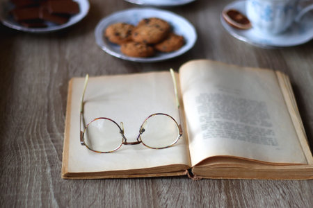 Cup of tea or coffee, plate of cookies, cup of blueberries, plate of chocolate, glass of juice, book, reading glasses, teapot, flowers and lit candles on the table. Brunch concept.の写真素材