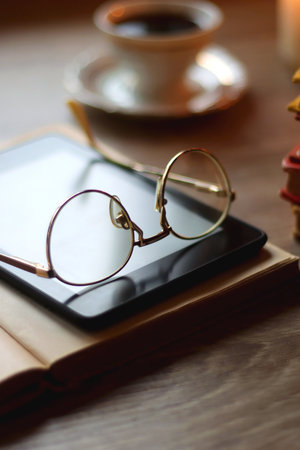 Cup of tea or coffee, plate of cookies, books, e-reader, pencil and lit candles on the table. Selective focus.の写真素材