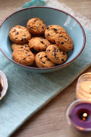 Books, reading glasses, e-reader, plate of chocolate pralines, bowl of cookies, cups of tea and lit candles on the table. Selective focus.の写真素材
