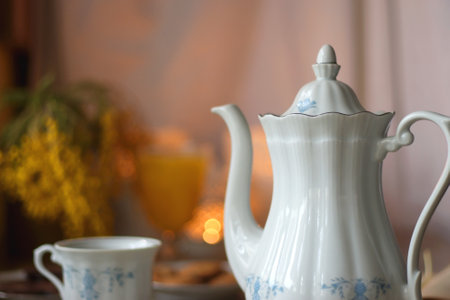 Cup of tea or coffee, plate of cookies, cup of blueberries, plate of chocolate, glass of juice, book, reading glasses, teapot, flowers and lit candles on the table. Brunch concept.の写真素材