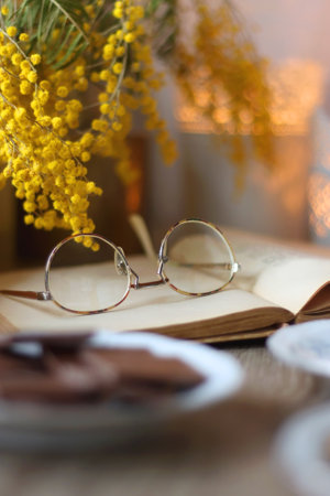 Cup of tea or coffee, plate of cookies, cup of blueberries, plate of chocolate, glass of juice, book, reading glasses, teapot, flowers and lit candles on the table. Brunch concept.の写真素材