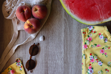 Floral yellow bikini, wicker bag, retro sunglasses, seashell, bag with peaches and cut watermelon on...