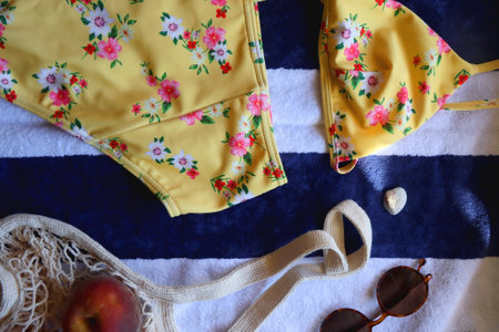 Floral bikini, sunglasses, straw bag, seashell and tote with peaches on striped beach towel. Top...