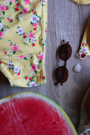 Floral yellow bikini, wicker bag, retro sunglasses, seashell, bag with peaches and cut watermelon on...