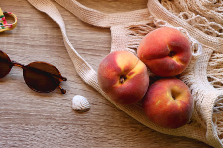Floral yellow bikini, wicker bag, retro sunglasses, seashell, bag with peaches and cut watermelon on wooden background. Top view, copy space.の写真素材
