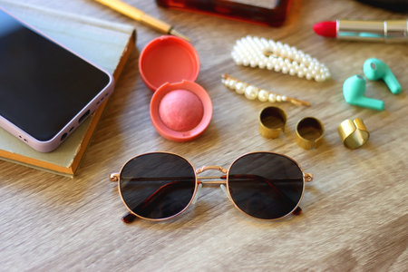 Handbag, sunglasses, beauty products, pearl hair clips, rings, pen, earbuds, book and phone on wooden background. Selective focus.の写真素材