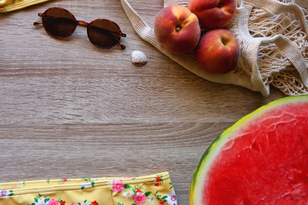 Floral yellow bikini, wicker bag, retro sunglasses, seashell, bag with peaches and cut watermelon on...
