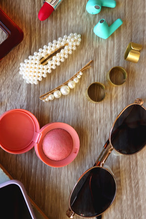 Handbag, sunglasses, beauty products, pearl hair clips, rings, pen, earbuds, book and phone on...