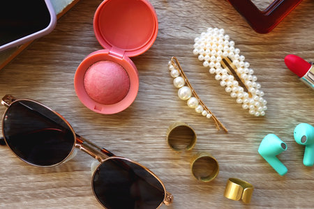 Handbag, sunglasses, beauty products, pearl hair clips, rings, pen, earbuds, book and phone on...