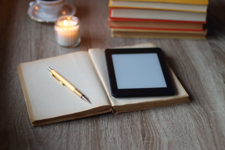 Cup of tea or coffee, plate of cookies, books, e-reader, pencil and lit candles on the table. Selective focus.の写真素材