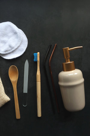 Fabric food bag, reusable cotton pads, wooden spoon, glass nail file, wooden toothbrush, reusable metal straws and ceramic soap dispenser on dark background.の写真素材