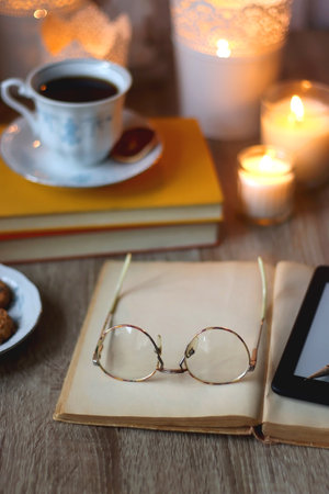 Cup of tea or coffee, plate of cookies, books, e-reader, pencil and lit candles on the table. Selective focus.の写真素材