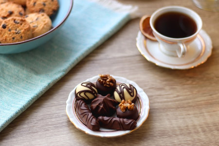 Plate of chocolate pralines, bowl of cookies, cups of tea, glasses of juice and lit candles on the...