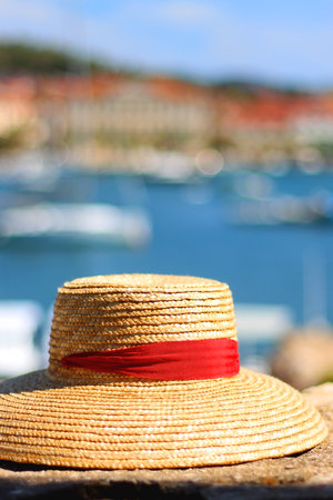 Fashionable straw hat on the stone wall. Picturesque Mediterranean town in the background. Selective focus.の写真素材