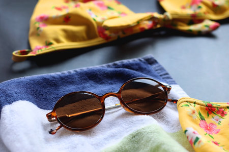 Yellow floral bikini, straw hat, striped towel and sunglasses on dark background. Selective focus.の写真素材