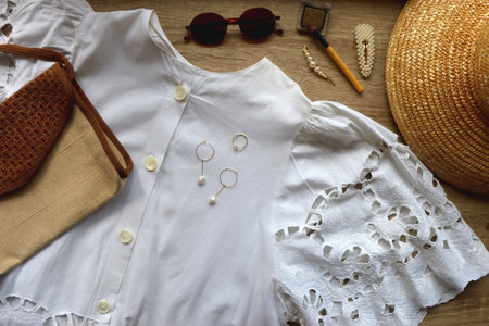 White lace blouse, straw hat, vintage bag and various accessories on wooden background. Summer...