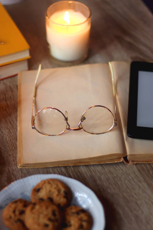 Cup of tea or coffee, plate of cookies, books, e-reader, pencil and lit candles on the table. Selective focus.の写真素材