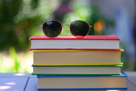 Stack of colorful hardcover books and sunglasses in the garden. Summer reading concept. Selectvie focus, colorful background.の写真素材