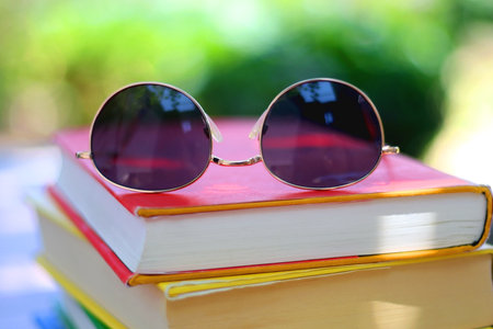 Stack of colorful hardcover books and sunglasses in the garden. Summer reading concept. Selectvie focus, colorful background.の写真素材
