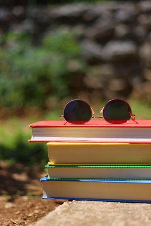 Stack of colorful hardcover books and sunglasses in the garden. Summer reading concept. Selectvie focus, colorful background.の写真素材