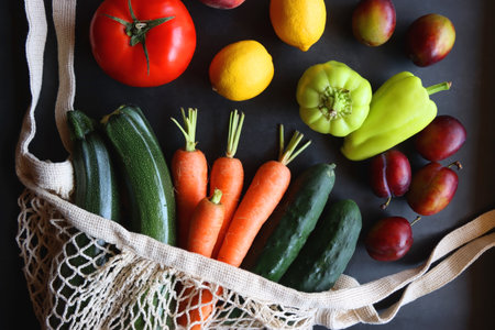 Mesh bag with fresh seasonal fruit and vegetable. Top view, dark background.の写真素材