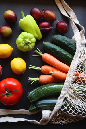 Mesh bag with fresh seasonal fruit and vegetable. Top view, dark background.の写真素材