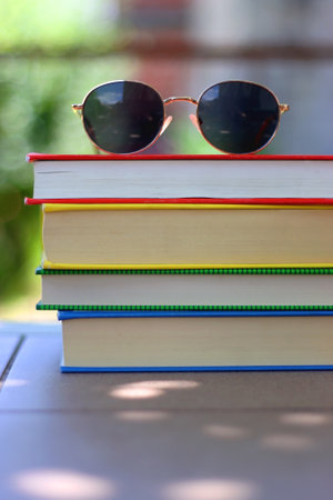 Stack of colorful hardcover books and sunglasses in the garden. Summer reading concept. Selectvie focus, colorful background.の写真素材
