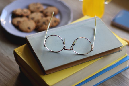 Plate of chocolate chip cookies, stack of books, reading glasses, orange soda, mobile phone and pen on the table. Hygge at home. Pastel colors, selective focus.の写真素材