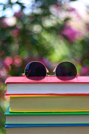 Stack of colorful hardcover books and sunglasses in the garden. Summer reading concept. Selectvie focus, colorful background.の写真素材