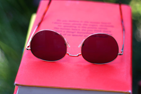 Stack of colorful hardcover books and sunglasses in the garden. Summer reading concept. Selectvie...