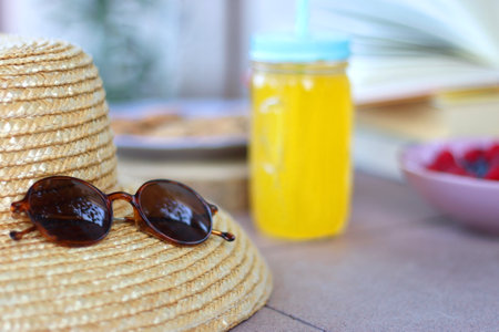 Straw hat, orange soda in the cactus shaped cup, bowl of fresh blueberreis and raspberries, plate of chocolate chip cookies, stack of books and sunglasses in the garden. Selectiveの写真素材
