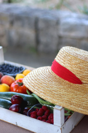 Crate with fresh homegrown fruit and vegetable and straw hat in the garden. Selective focus.の写真素材