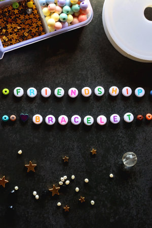 Friendship bracelet letter beads and various other jewelry making supplies on dark background. Top view.の写真素材