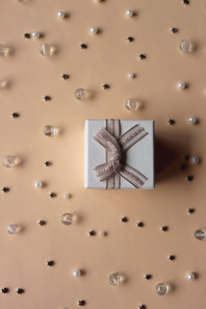 Small white present on neutral peachy background. Stars, pearls and beads in the background. Birthday or Christmas concept. Top view.の写真素材