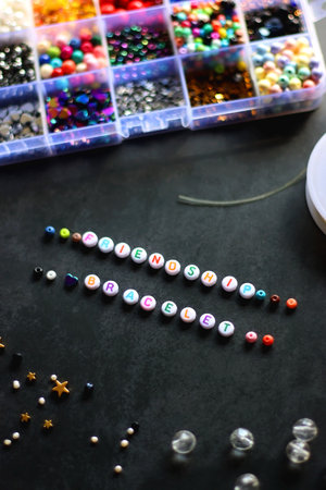 Friendship bracelet letter beads and various other jewelry making supplies on dark background....