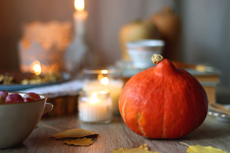Cup of tea or coffee, plate with desserts, dried oranges, bowl of grapes, scented candles, vintage books, pumpkins and autumn leaves on the table. Autumnal hygge. Selective focus.の写真素材