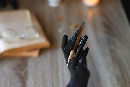 Vintage books, reading glasses, gold pen, hand model, gold jewelry, scented candles, flowers, chess pieces and cup of tea or coffee on the table. Dark academia concept.の写真素材