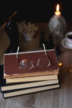 Vintage books, reading glasses, gold pen, hand model, gold jewelry, scented candles, flowers, chess pieces and cup of tea or coffee on the table. Dark academia concept. Selective fの写真素材