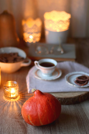 Vintage books, reading glasses, cup of tea or coffee, bowl of cookies, pumpkin and lit candles on the table. Hygge at home, fall atmosphere. Selective focus.の写真素材
