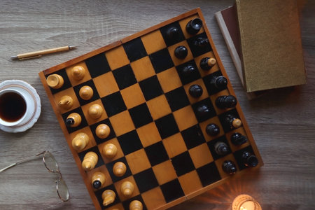 Vintage wooden chessboard, books, glasses, pen, cup of tea or coffee and scented candle on the...