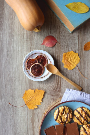 Cup of tea or coffee, plate with cookies and chocolate, dried oranges, bowl of grapes, vintage books, pumpkins and autumn leaves on the table. Autumnal hygge. Top view.の写真素材