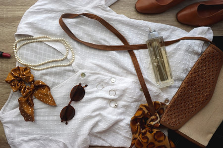 White blouse, denim skirt, brown shoes, vintage bag, leopard print scarf, pearl necklace, scrunchie, silver rings, perfume and lipstick on wood background. Retro, elegant outfit.の写真素材
