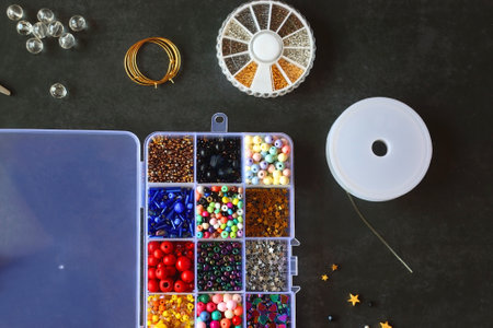 Box with colorful beads, string, wire, chain, scissors, pliers and hammer on dark background. Various jewelry making supplies. Top view.の写真素材
